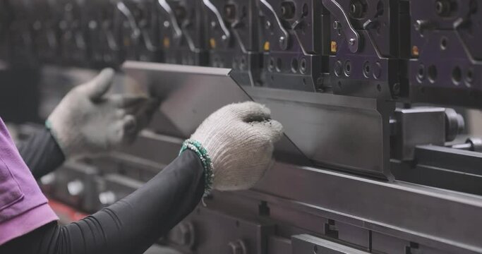 Hydraulic sheet metal bending machine. A worker bends a metal part in a machine. Metal processing