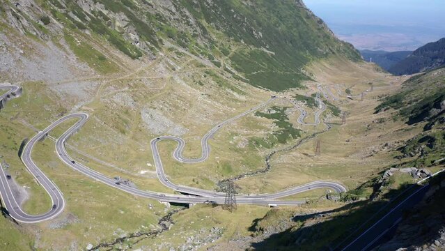 Video of a drone flying over a man and woman standing on the edge of a cliff overlooking the famous Transfagarasan mountain road in Romania. A couple enjoying the beauty of nature.