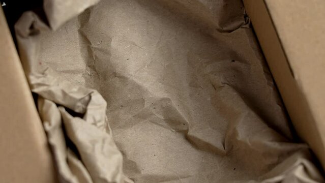 Post cardboard box with crumpled brown paper filler ready for packaging close up. Empty delivering container. Rotation