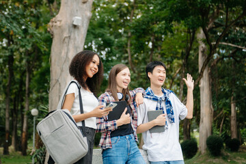 Three young college students is reading a book while relaxing sitting on grass in a campus park with her friends.