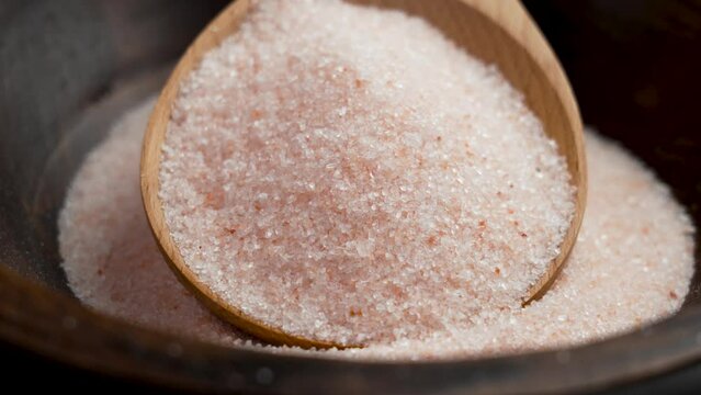 Pile of pink Himalayan salt in wooden spoon close up. Exotic cuisine ingredients. Rotation