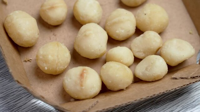 Peeled ready-to-eat macadamia nuts in market paper pack close up on a white board. Rotation