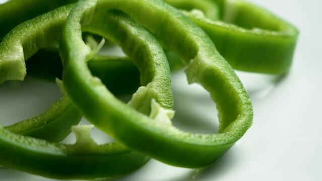 Sliced organic green bell peppers on a white ceramic plate close up. Rotation