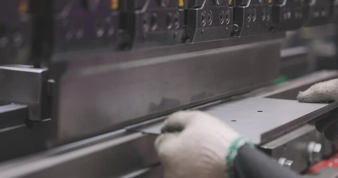 Hydraulic sheet metal bending machine. A worker bends a metal part in a machine. Metal processing