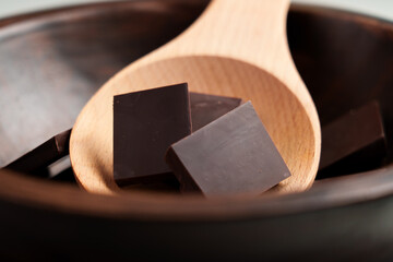 Pieces of dark chocolate from pure cacao ingredients in bowl with wooden spoon
