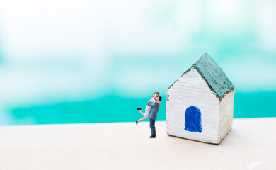 Miniature couple and wooden house model over blurred background, handmade miniature house for small...