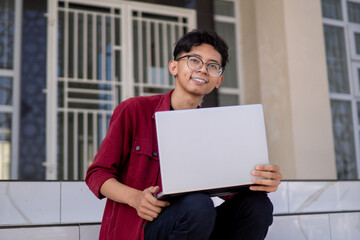 Portrait of Asian college student using laptop looking to camera. A man working with a laptop computer at campus