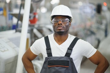 African male engineer. Control a material production machine system, working in a plastic and steel...