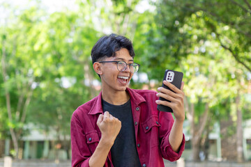 Asian man showing surprised expression while looking to his phone. Excited and happy man looking to mobile phone