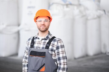 Portrait of man loader in uniform near big bag of coffee beans or wheat, nuts in warehouse of...