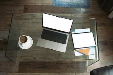 Top view laptop with blank screen, digital tablet, document and coffee cup on glass table in living room