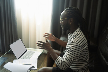 Side view of young African man talking on video call on laptop at home