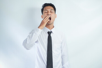 Lazy tired  young businessman yawning and feeling sleepy, he is covering his mouth with his hand
