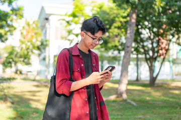 Fototapeta premium Young Asian man using smartphone with happy expression. A male smiling while holding his phone at the public park
