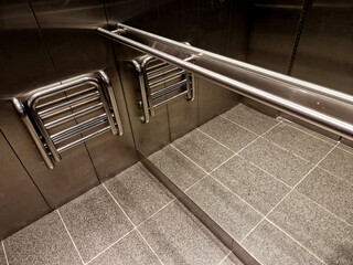 stainless steel elevator cabin interior with hardwood oak floor and mirror paneling. handrail and...