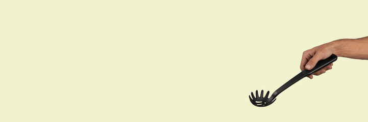 Black male hand holding plastic kitchen skimmer on light green banner