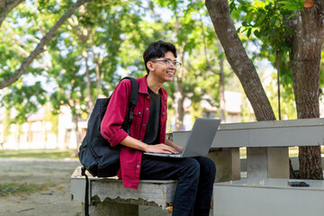 Fototapeta premium Asian college student sitting and focused to his laptop screen. Asian young male sitting outdoors using laptop computer, typing, working freelance project