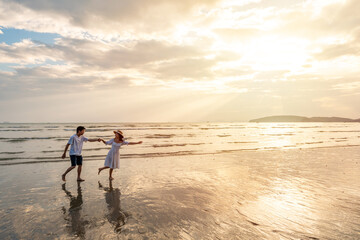 Young woman traveler holding man's hand and looking beautiful sunset on the beach, Couple on vacation in summer concept