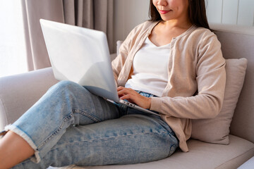 Young Asian woman relaxing and using laptop on a sofa at home in