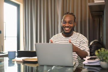 Positive African man looking at laptop talking to online video call distant speaking with friends