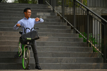 Smiling businessman with his bicycle in front of the building and checking time on wristwatch
