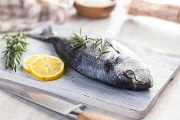Fresh sea bream fish on cutting board on kitchen table. - 791404697