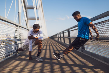 Two african-american friends are exercising on the bridge in the city. They are warming up for jogging. - 791406093