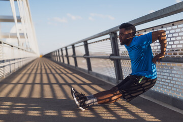 Young african-american man is exercising on the bridge in the city. He is doing reverse push-ups. - 791406229
