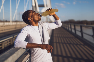 Portrait of young african-american man who is drinking water and relaxing after jogging. - 791406249
