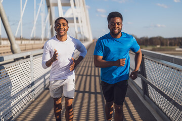 Two african-american friends are jogging on the bridge in the city.