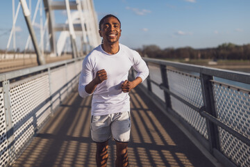 Young african-american man is jogging on the bridge in the city. - 791406460