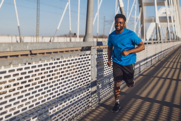 Young african-american man is jogging on the bridge in the city. - 791406462