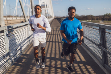 Two african-american friends are jogging on the bridge in the city. - 791406465