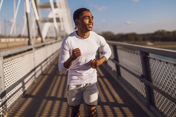 Young african-american man is jogging on the bridge in the city. - 791406467