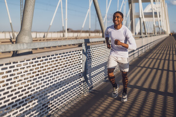 Young african-american man is jogging on the bridge in the city. - 791406469
