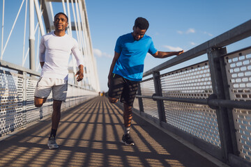 Two african-american friends are exercising on the bridge in the city. They are warming up for jogging. - 791406471