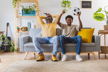 Cheerful man and grandson watching soccer match together at home