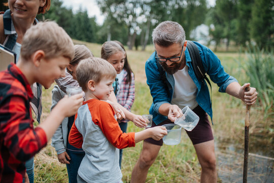 Teacher showing lake water to school children, during field teaching class. Outdoor active education helping young student to learn about ecosystem.