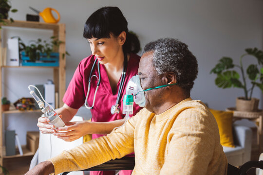 Home caregiver giving painkiller to senior man in oxygen mask
