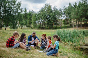 Teacher showing sample of lake water to school children, during field teaching class. Outdoor active education helping young student to learn about ecosystem.