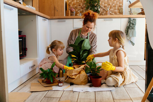 Daughters helping mother in planting plants at home