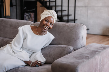 Joyful woman in headwrap seated on couch, home setting