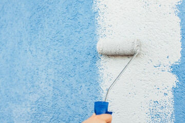 Hand of girl painting white color on wall using roller