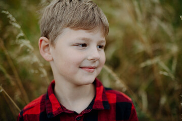 Portrait of young boy standing in nature, in the middle of tall grass, headshot. Copy space.