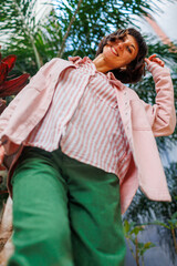Young beautiful smiling hipster woman in fashionable summer clothes. Portrait of a broadly smiling girl. The girl wears a pink shirt and green pants.