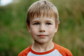 Portrait of young boy standing in nature, in the middle of tall grass, headshot. Copy space.