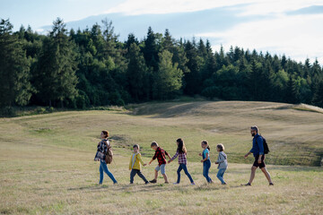 Young students walking across meadow during biology field teaching class, holding hands. Dedicated teachers during outdoor active education teaching about ecosystem, ecology.