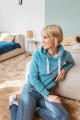 Happy Middle-Aged Woman Sitting on Floor in Cozy Living Room - 791411215