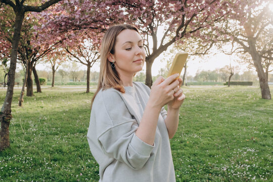 Woman using smart phone with cherry blossoms in background at park