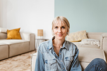 Smiling Middle-Aged Blonde Woman Sitting on Living Room Floor - 791411817